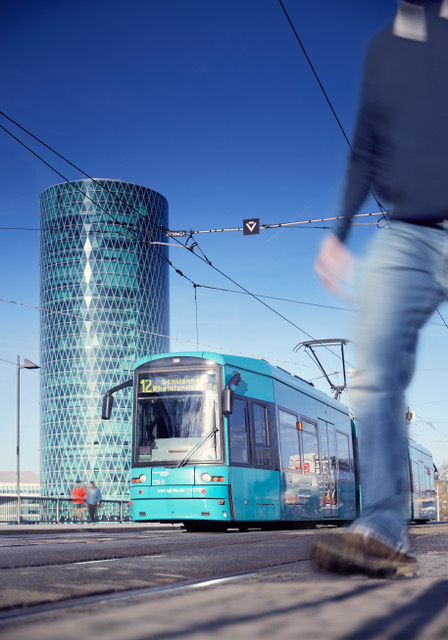 Die VGF-Straßenbahn der Linie 16 fährt bei strahlendem Sonennschein am Gebäude "Westhafen Tower" in Frankfurt vorbei.