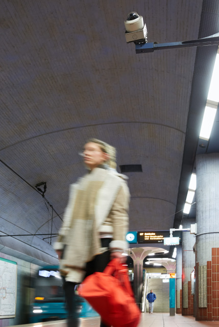 Frau mit einer roten Reisetasche steht an einer unterirdischen U-Bahn-Haltestelle