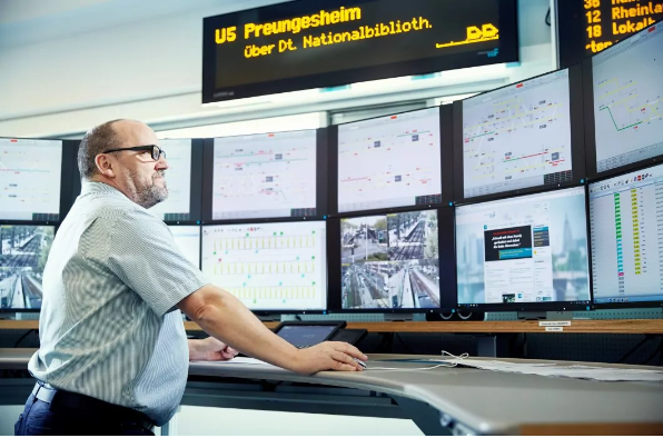 Ein Mitarbeiter der Leitstelle steht an einem Arbeitsplatz mit vielen Bildschirmen.