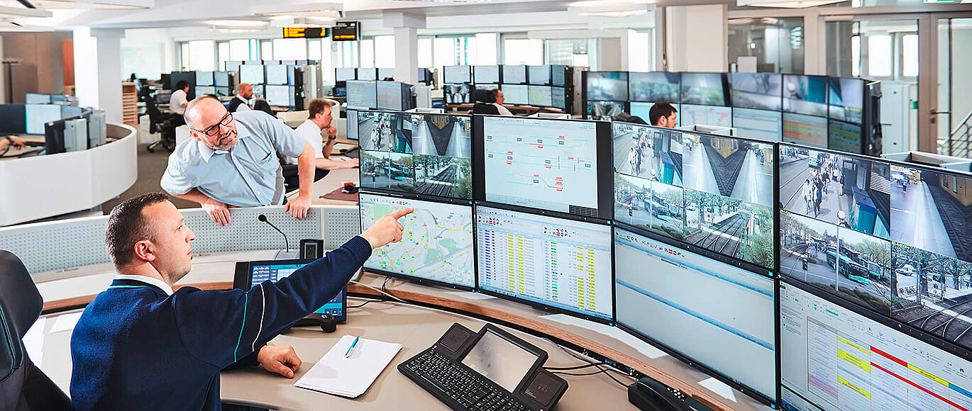 Zwei Mitarbeiter der Leitstelle an einem Arbeitsplatz der mit vielen Bildschirmen.