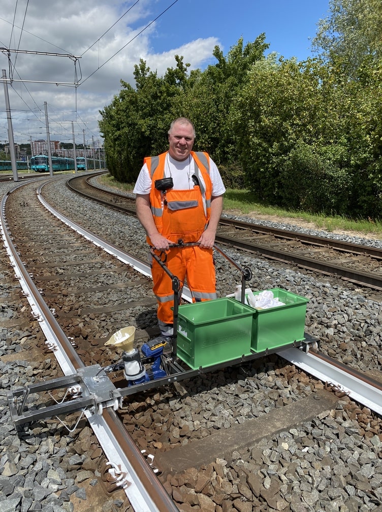 Mitarbeiter bedient die Gleislackiermaschine und streicht die Schienen mit weißer Farbe gegen Hitzeschäden.