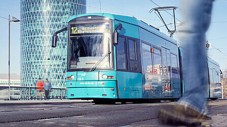 Die VGF-Straßenbahn der Linie 16 fährt bei strahlendem Sonennschein am Gebäude "Westhafen Tower" in Frankfurt vorbei.