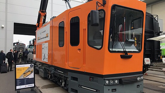 Das Gleisarbeitsfahrzeug GAF: ein Schienenfahrzeug in Orange mit einem Anhänger und vielen technischen Elementen.