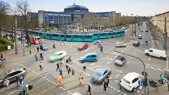 Eine große Straßenkreuzung mit Ampeln auf der Fußgänger, Autos und eine Straßenbahn gleichzeitig unterwegs sind.