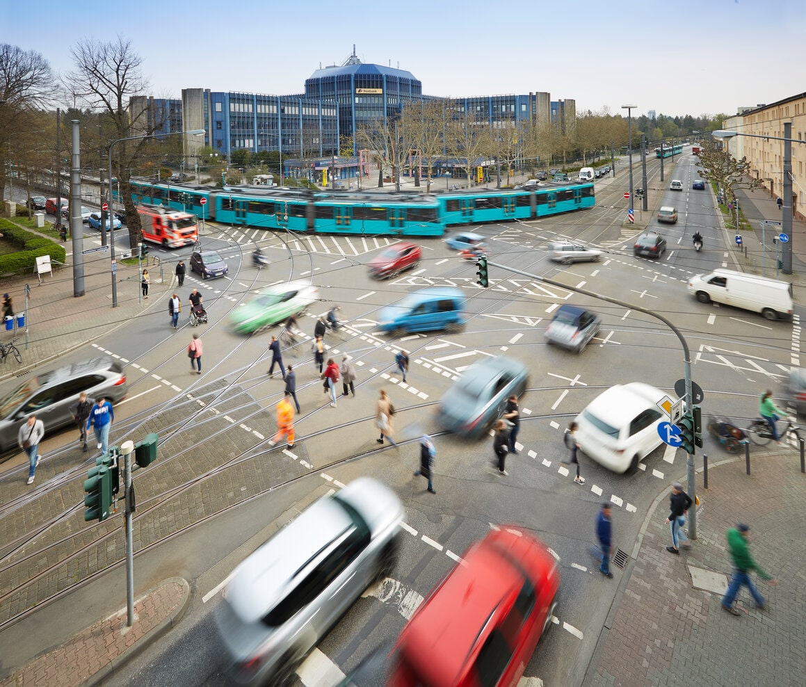 Straßenkreuzung mit Autos, Fußgängern und U-Bahnen.
